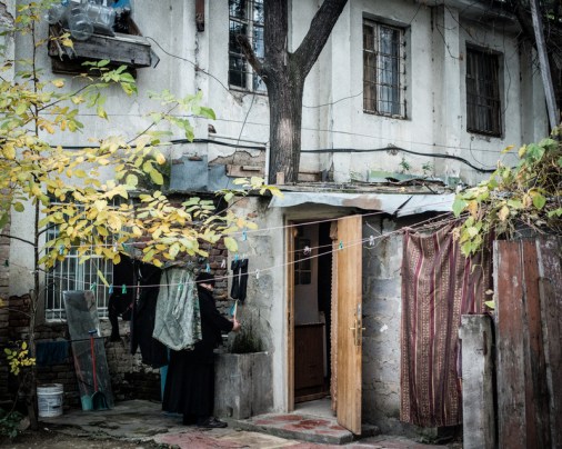 Binanın sakinlerinden biri, girişteki çeşmede kıyafetlerini yıkıyor