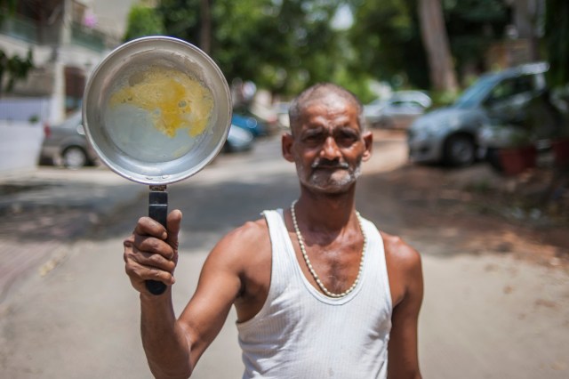 Hindistan’ın Yeni Delhi kentinde 49 yaşındaki Ajay Adav, asfaltta pişirdiği omleti gösteriyor